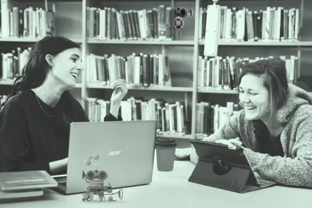Photo. Two happy students with desktop computers in a library.