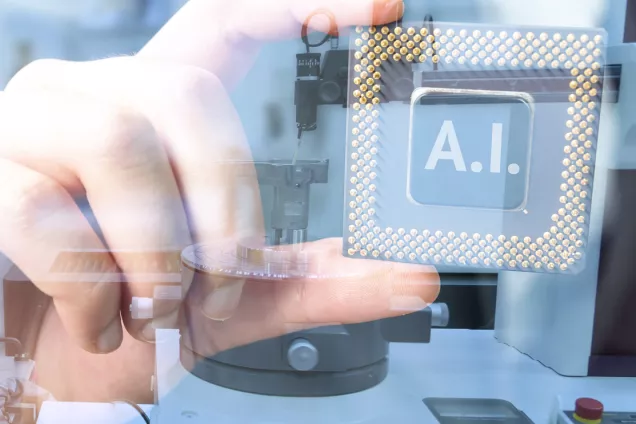 Bild. Hand som håller ett chip med texten ''AI'' på, robotarm i bakgrunden. 